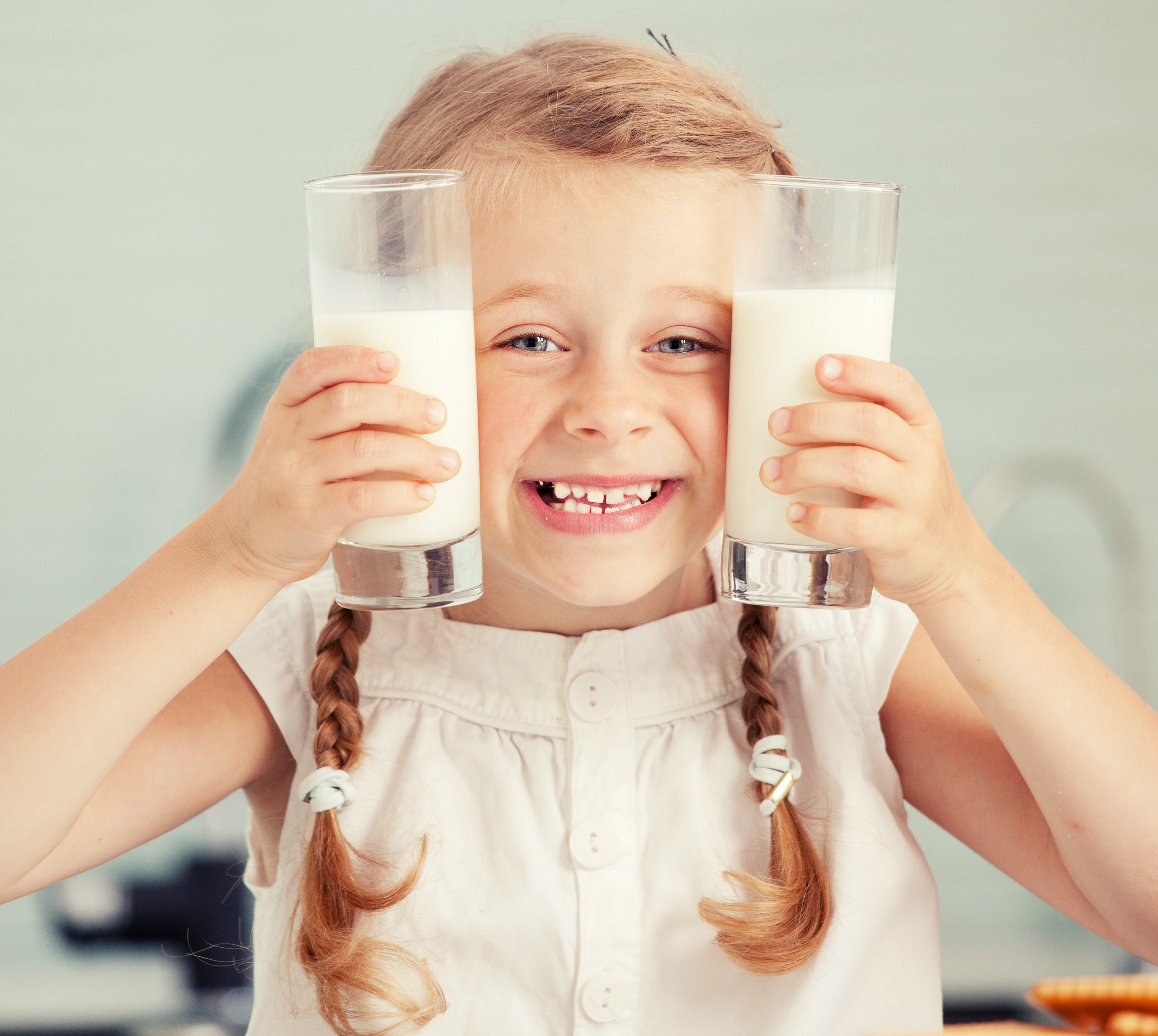 Little girl holding two large glasses of milk up to either side of her face