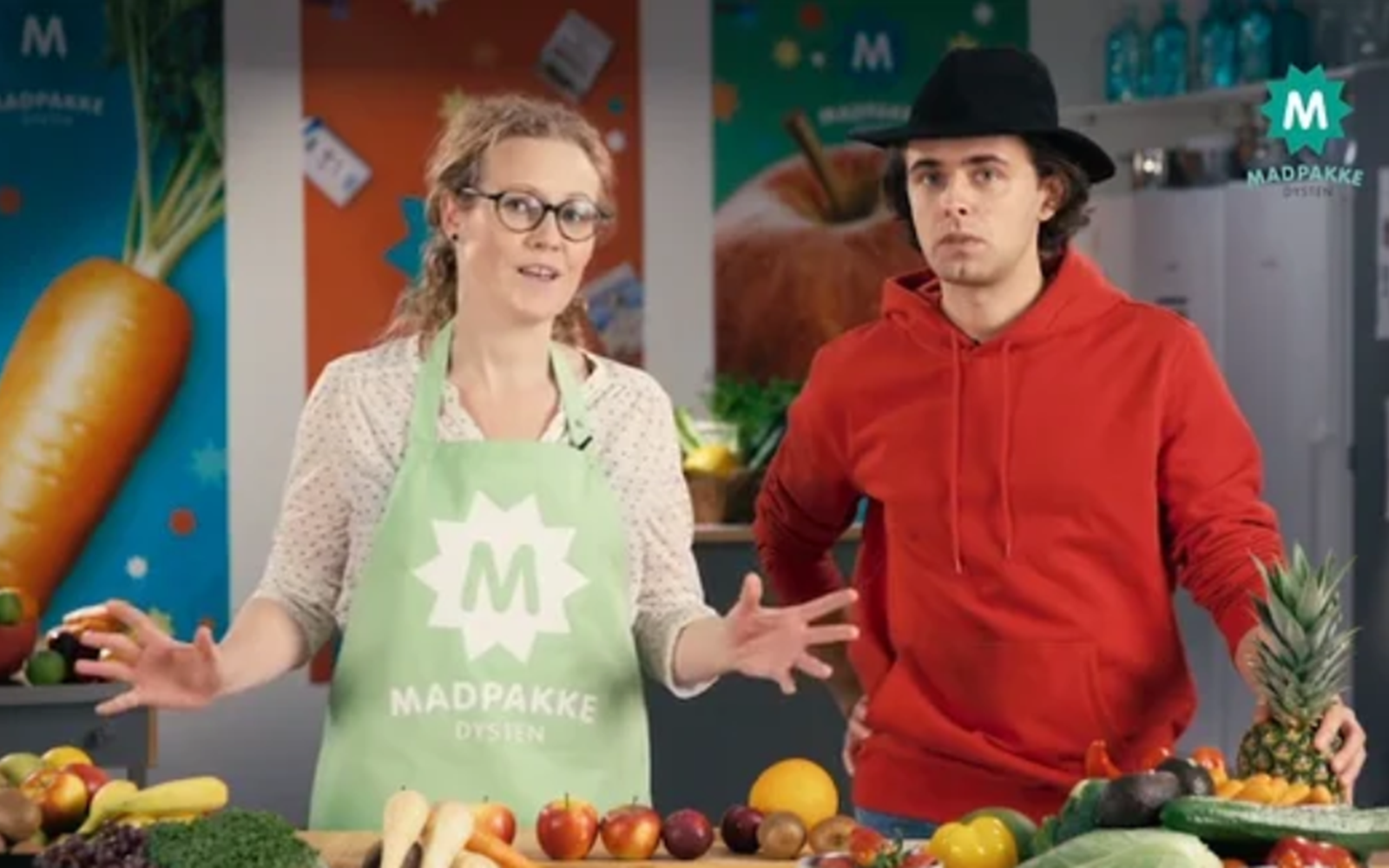 Man and woman in a kitchen surrounded by fresh fruits and vegetables