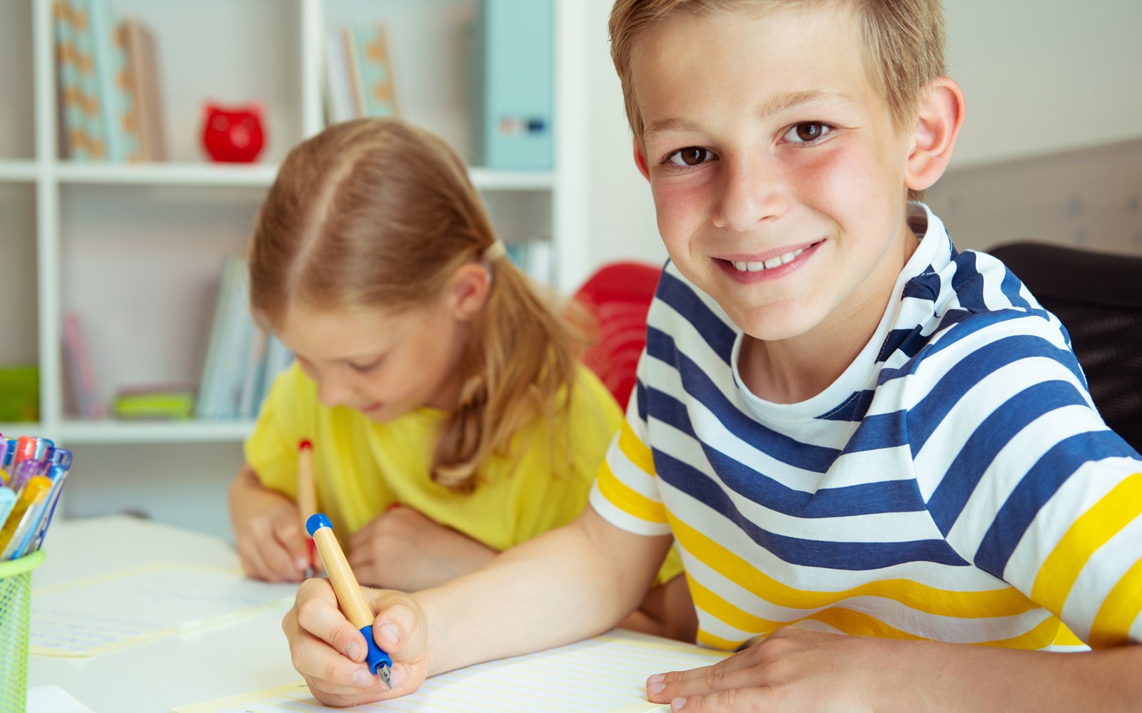 Boy and girl doing school work at a table, the boy smiling at the camera