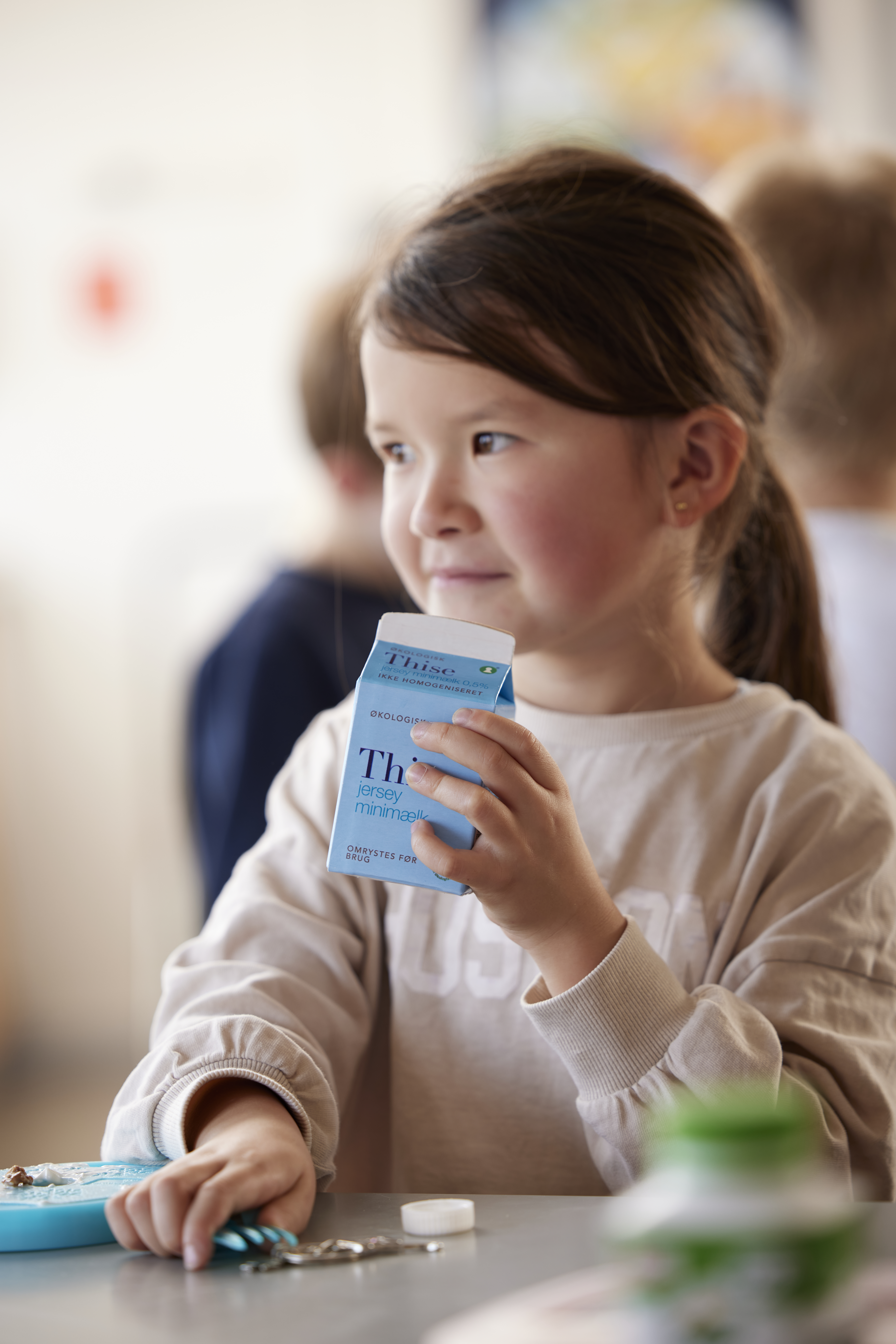 Brown haired little girl looking to the side with a school milk in her hands