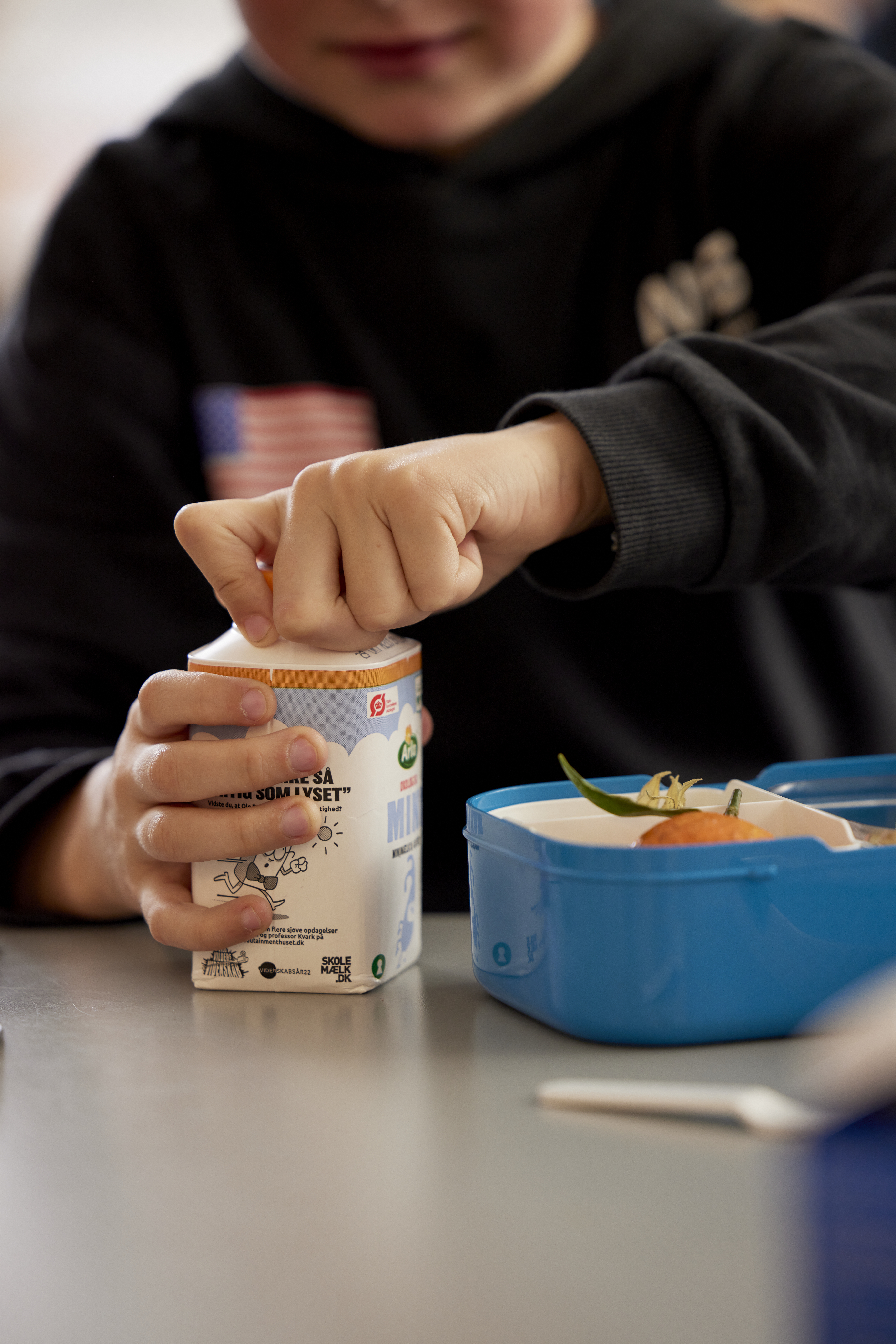 The hands of a boy opening a school milk carton