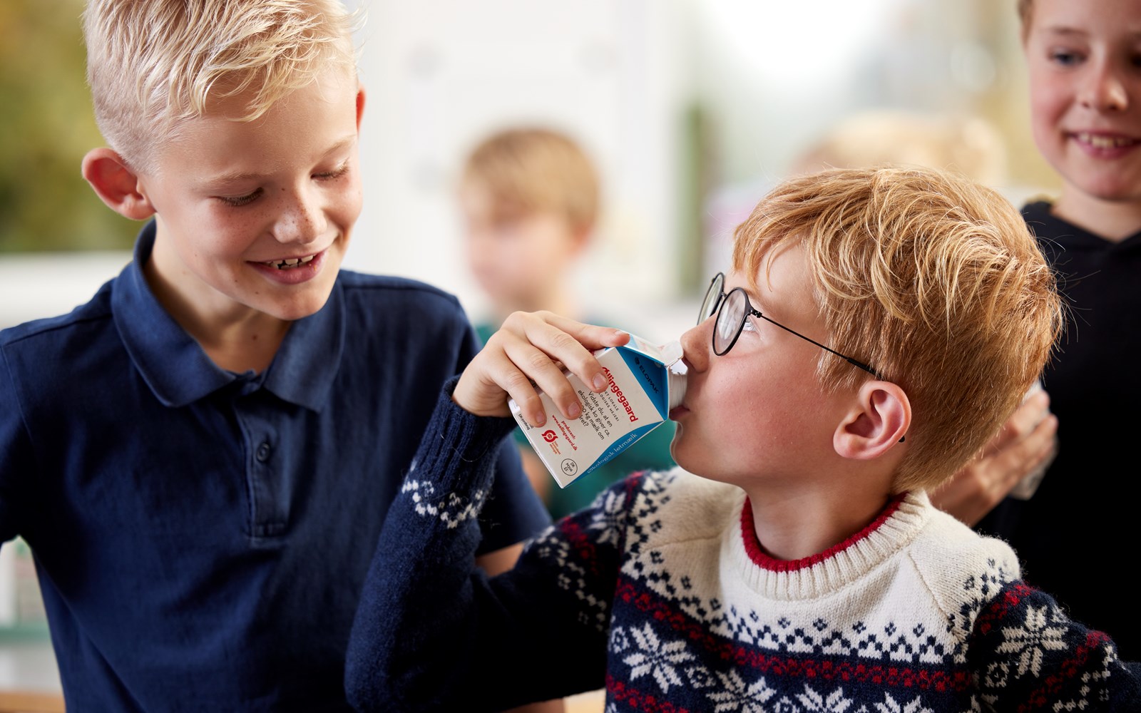 Two boys looking at each other, one of them drinking milk from a school milk carton